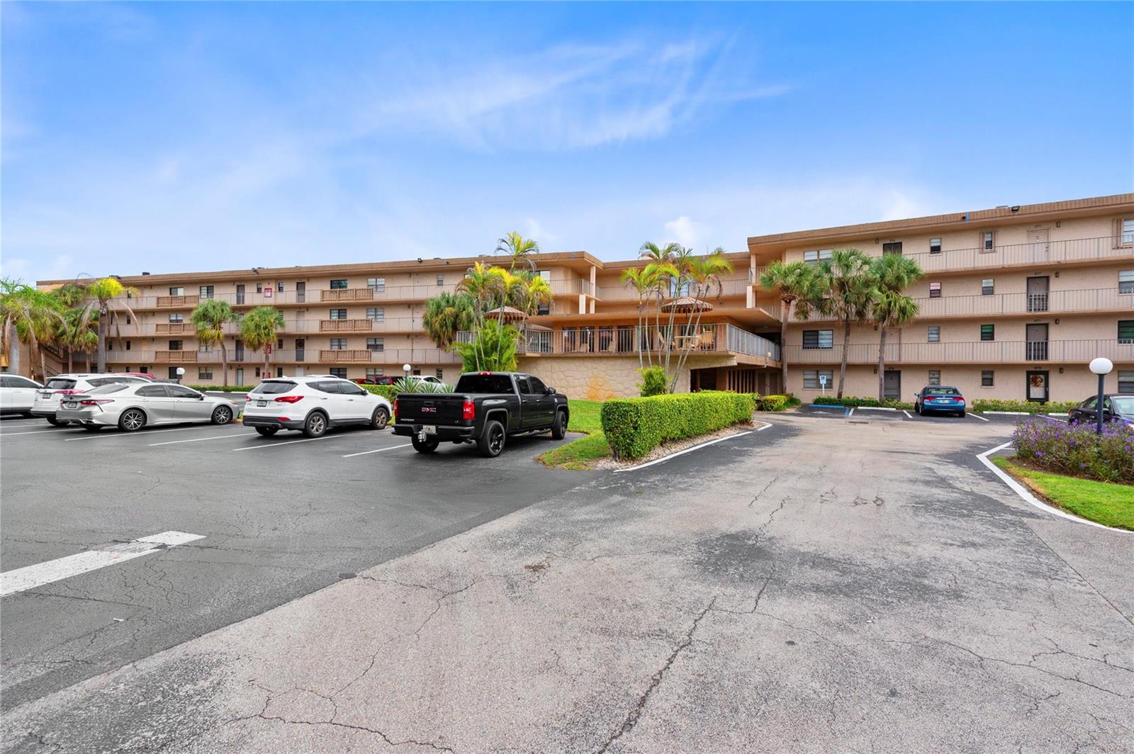 A multi-story apartment building with a parking lot in the foreground and palm trees — 9300 SW 8th Street # 102, Boca Raton FL 33428, BOCA RATON, FL