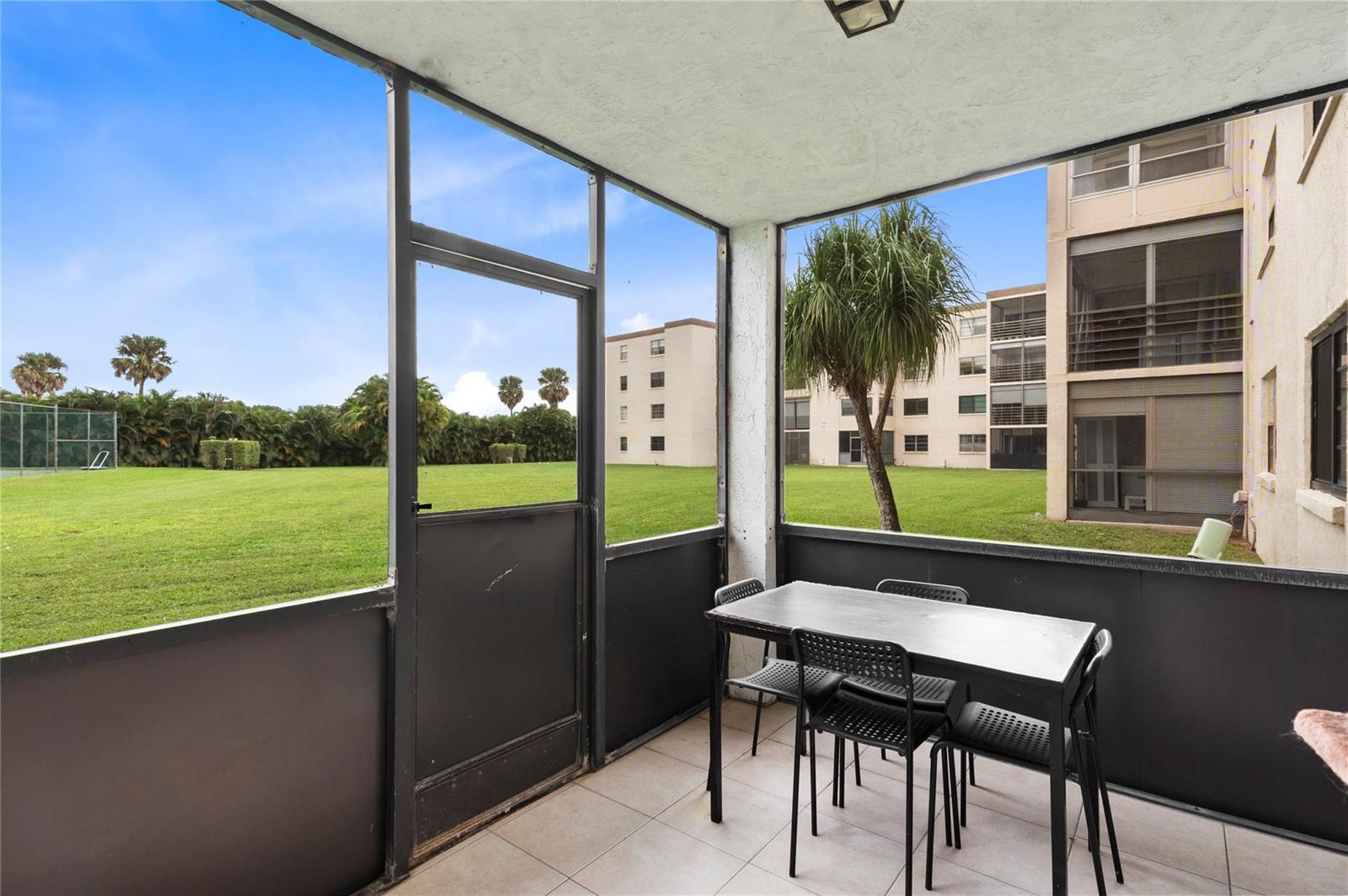 A screened-in patio features a dining table and chairs overlooking a grassy courtyard — 9300 SW 8th Street # 102, Boca Raton FL 33428, BOCA RATON, FL