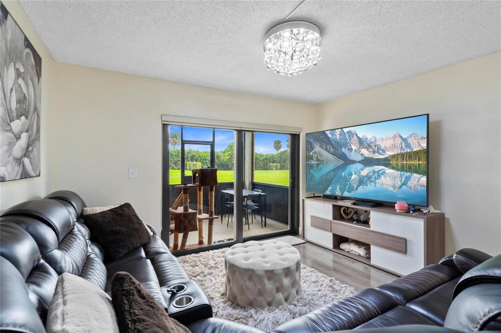 A living room features a leather sofa, a tufted ottoman, and a sliding glass door — 9300 SW 8th Street # 102, Boca Raton FL 33428, BOCA RATON, FL