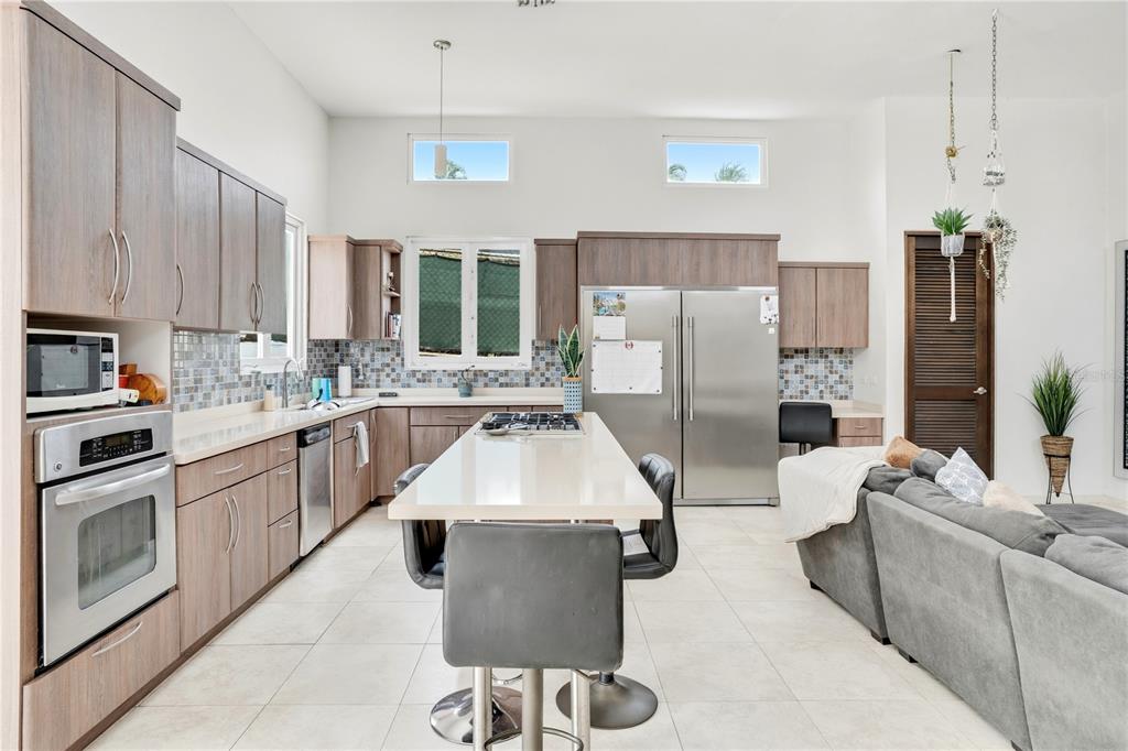 A modern kitchen features wood-toned cabinetry, stainless steel appliances, and a central island with seating — 12-11 CALLE SEGOVIA, GUAYNABO, PR