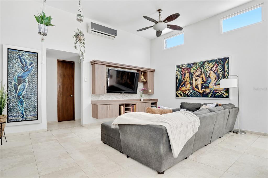 A living room features a grey sectional sofa, a wall-mounted television, and two large paintings — 12-11 CALLE SEGOVIA, GUAYNABO, PR