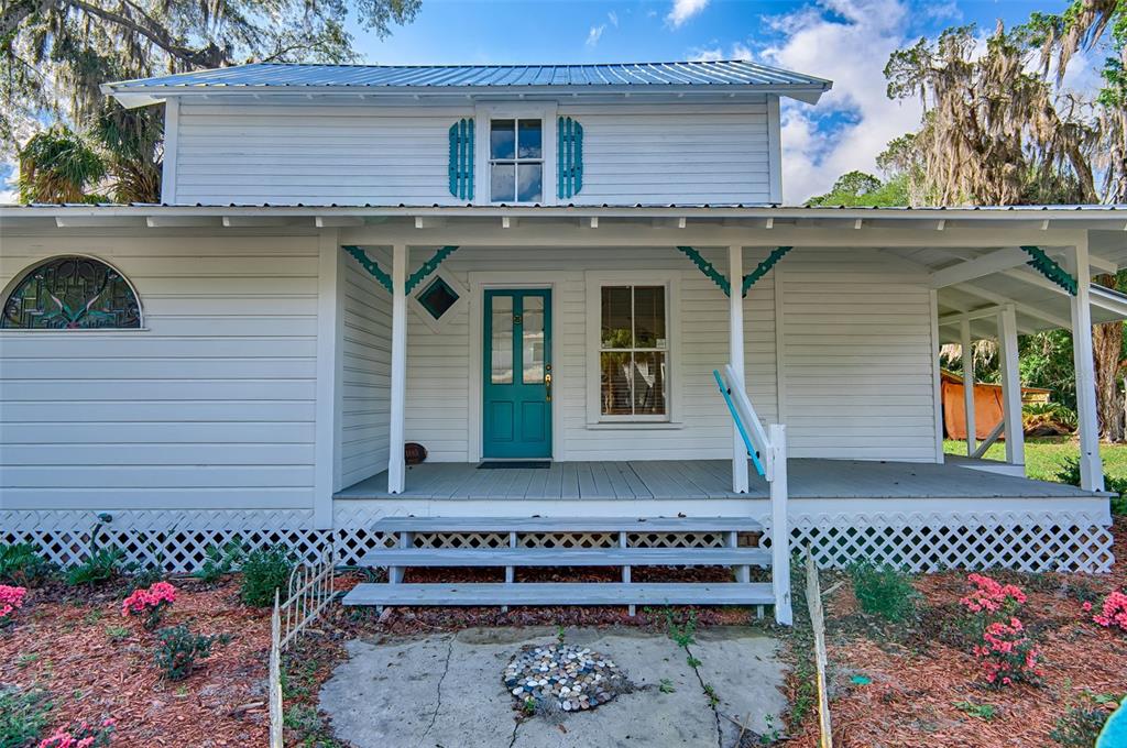 A white house with a teal front door, a covered porch, and a metal roof — 25415 NE STATE ROAD 26, MELROSE, FL