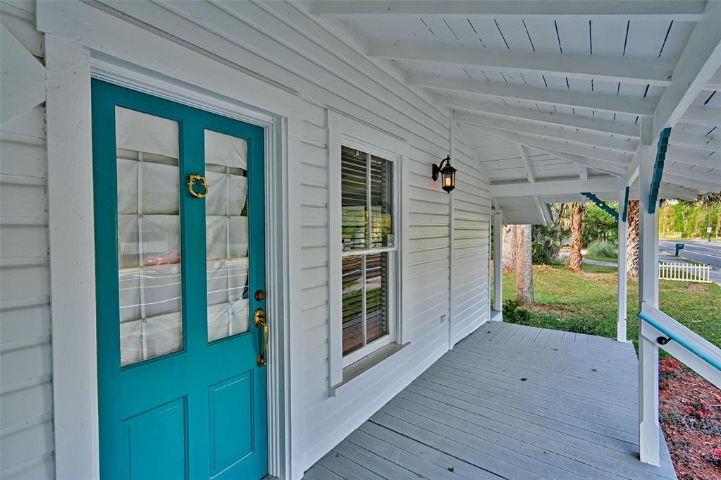 A teal front door with a brass knocker opens onto a covered wooden porch — 25415 NE STATE ROAD 26, MELROSE, FL