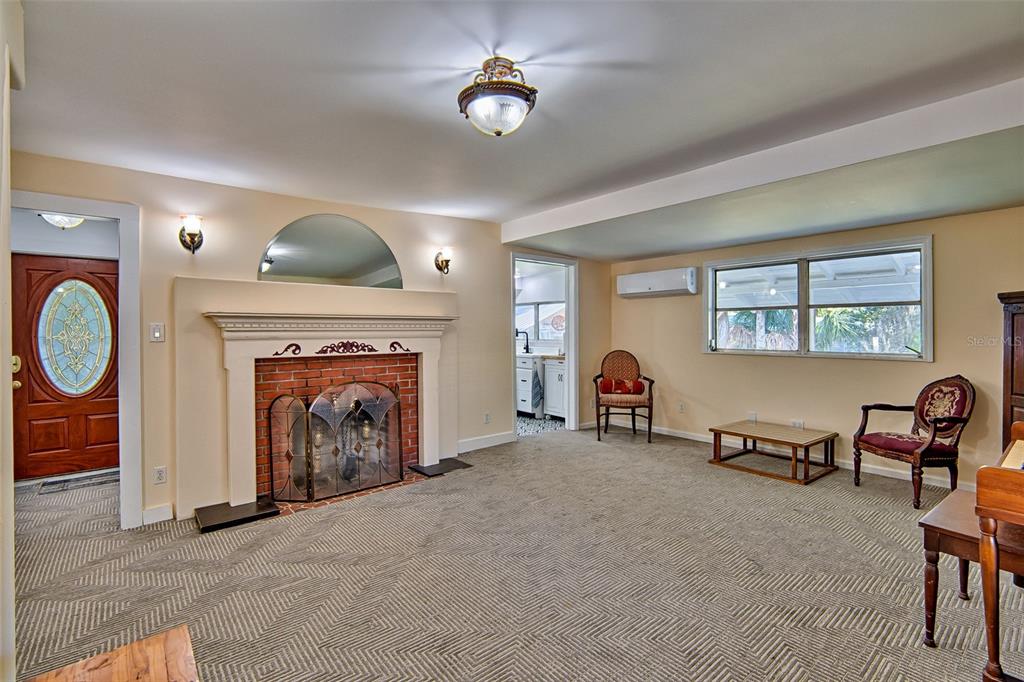 A living room features a brick fireplace, beige carpet, and a doorway leading to a kitchen — 25415 NE STATE ROAD 26, MELROSE, FL