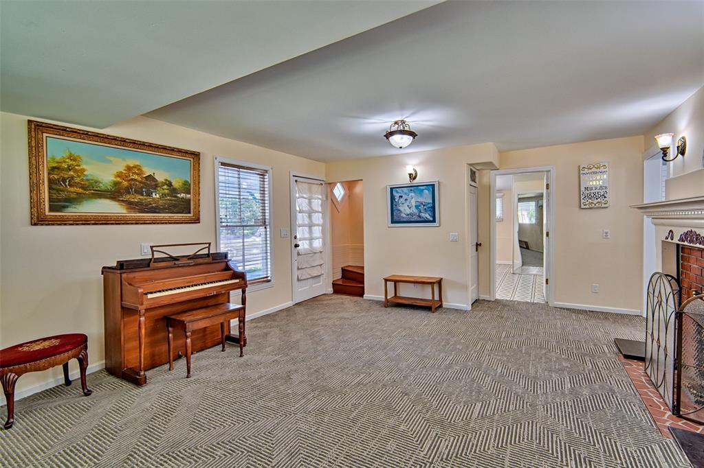A living room features a piano, patterned carpet, a brick fireplace, and a doorway — 25415 NE STATE ROAD 26, MELROSE, FL