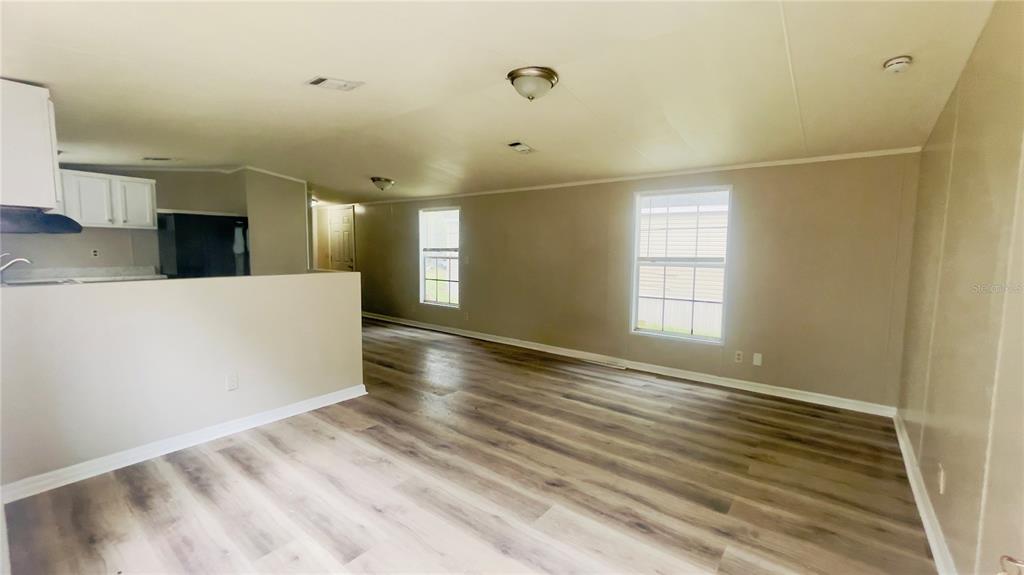 An open-concept living room features light wood-look flooring, beige walls, and a partial kitchen wall — 4053 NE 213TH TERRACE, WILLISTON, FL