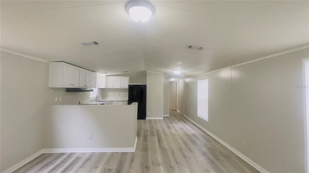 An open-concept kitchen and living area with light wood-look flooring and white cabinetry — 4053 NE 213TH TERRACE, WILLISTON, FL