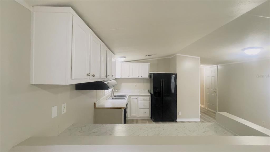 A kitchen features white cabinets, a black refrigerator, and a marble-patterned countertop — 4053 NE 213TH TERRACE, WILLISTON, FL