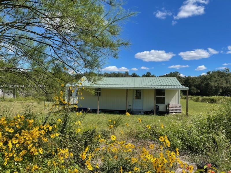 A light-colored, single-story house with a green metal roof sits in a grassy field — 3725 SW 162 St., Archer, FL, Gainesville FL 32618, GAINESVILLE, FL