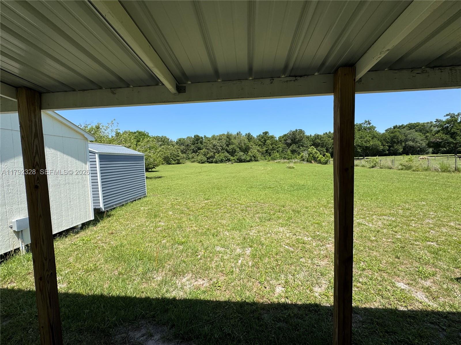 A view of a grassy backyard from under a covered porch with two wooden posts — 3725 SW 162 St., Archer, FL, Gainesville FL 32618, GAINESVILLE, FL