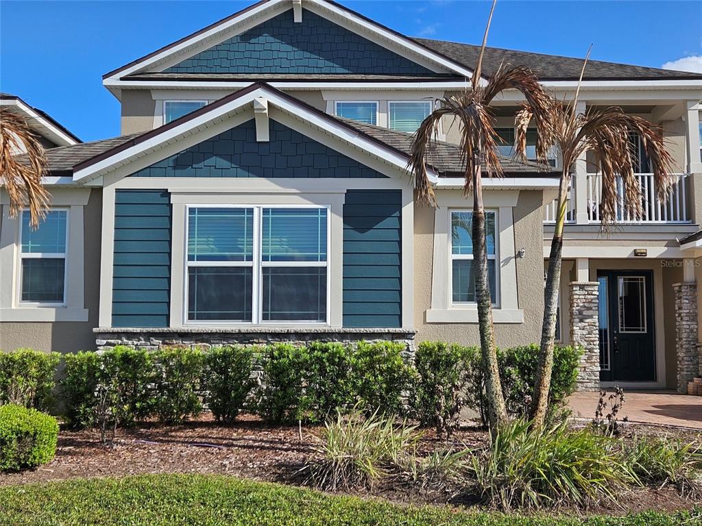 The exterior of a two-story house features blue shingle siding, stone accents, and palm trees — 2840 CHANTILLY AVENUE, KISSIMMEE, FL