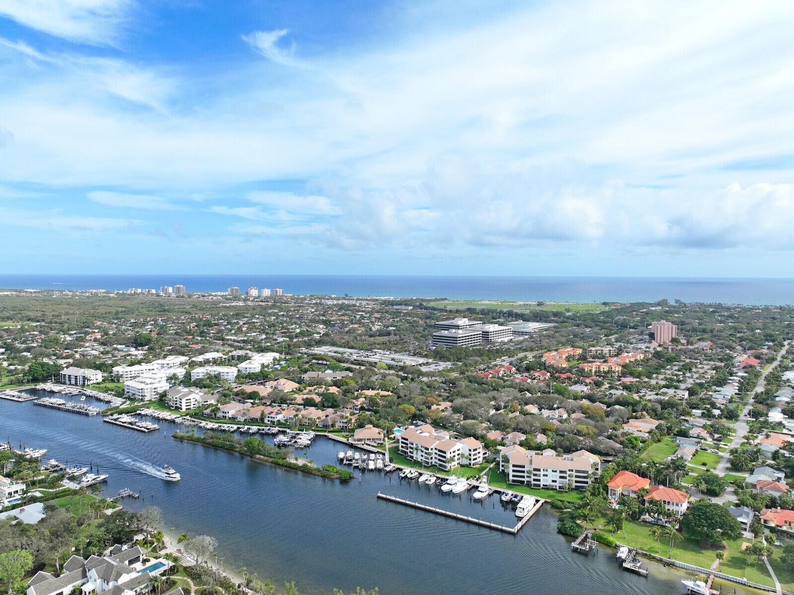 An aerial view shows a canal with docked boats winding through a coastal residential neighborhood — 215 Oak Harbour Drive, Juno Beach FL 33408, JUNO BEACH, FL