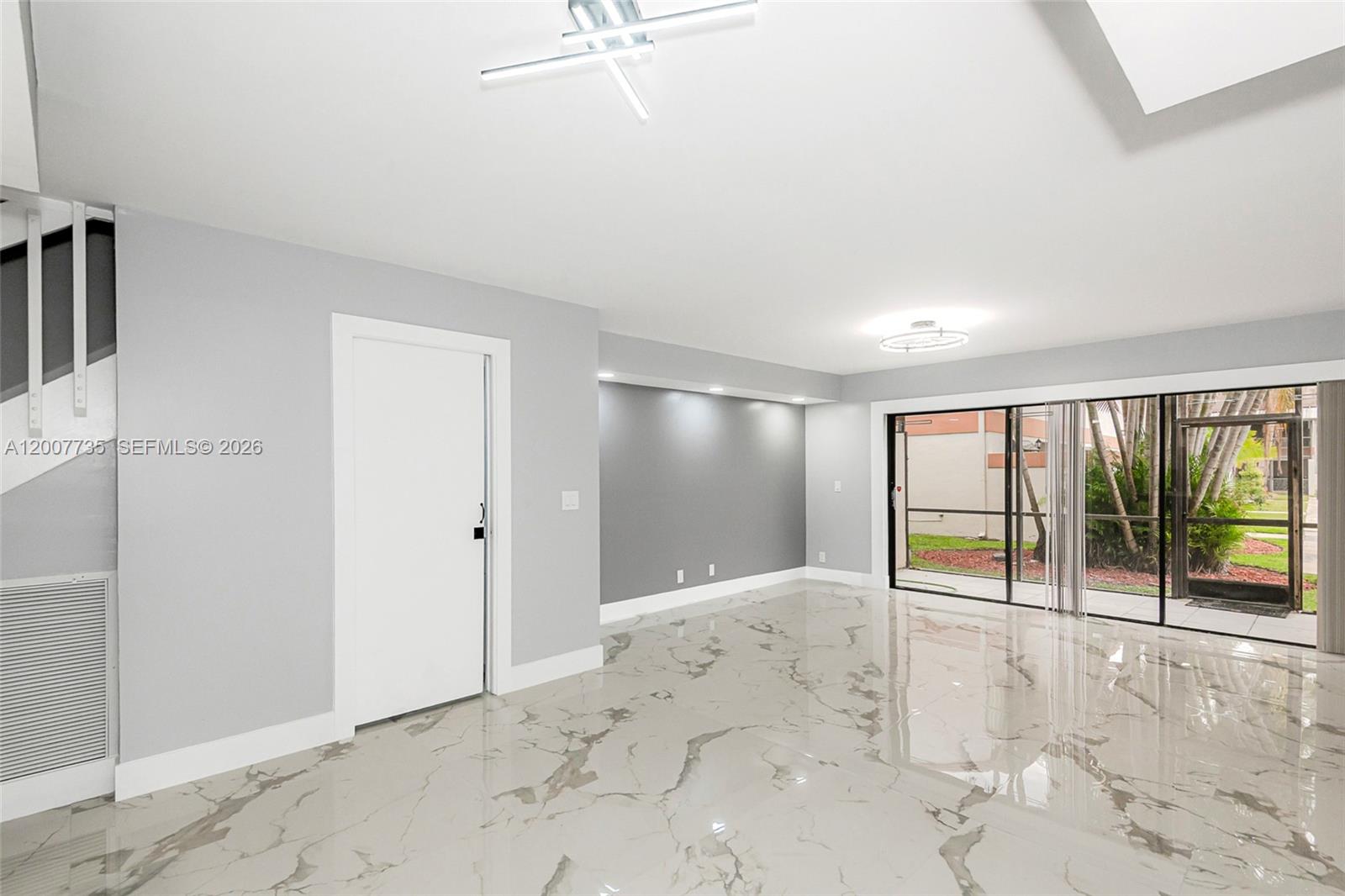 A bright living room features white marble floors, a grey accent wall, and sliding glass doors — 7111 SW 42nd Pl, Davie FL 33314, DAVIE, FL