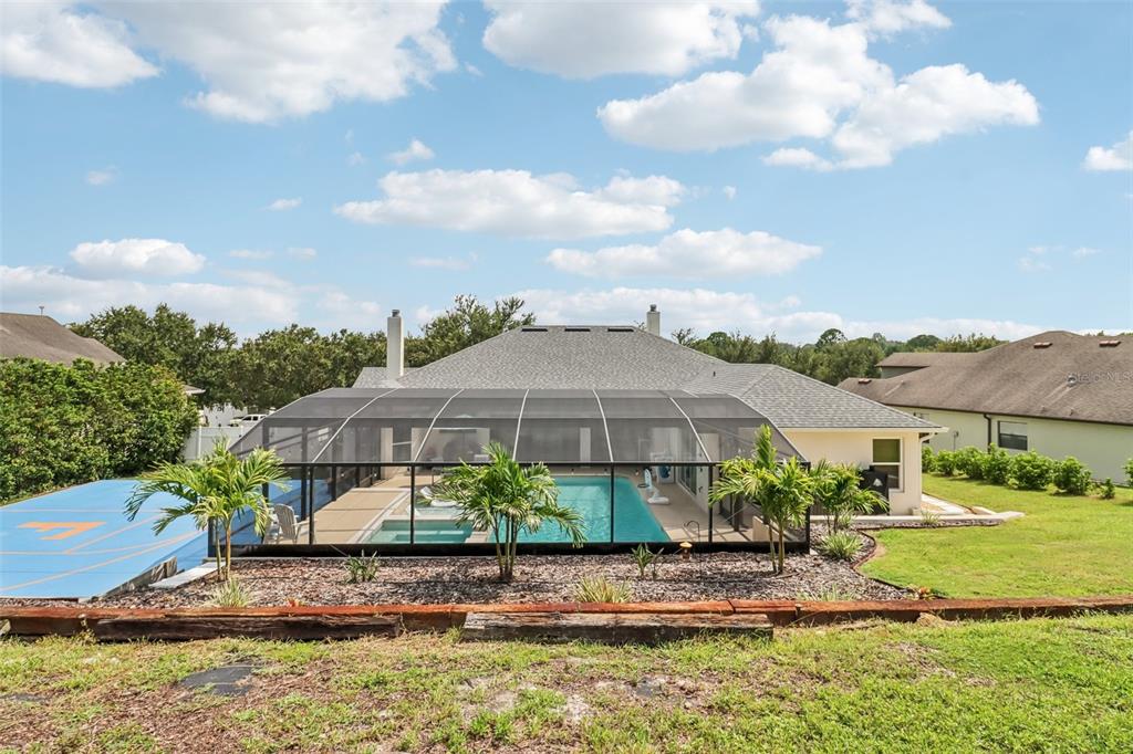 A backyard features a screened-in swimming pool, a blue sports court, and a grassy lawn — 225 GLEN ABBEY LANE, DEBARY, FL