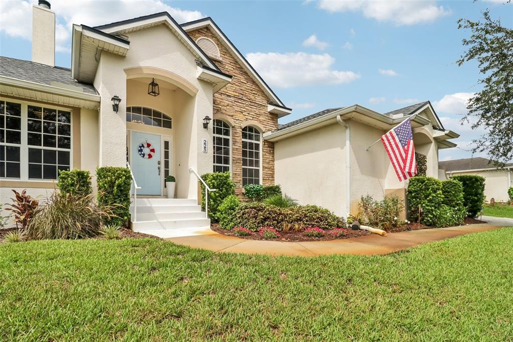 A single-story house with a stone facade, light-colored stucco, and an American flag displayed — 225 GLEN ABBEY LANE, DEBARY, FL