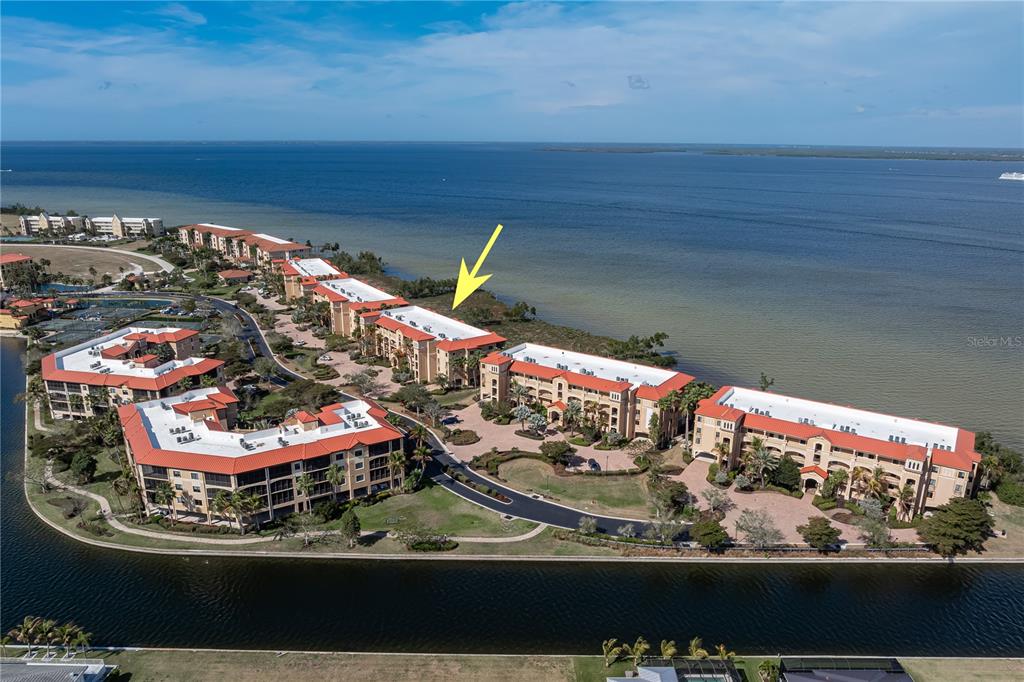 An aerial view shows a multi-story residential complex situated along a waterfront — 89 VIVANTE BOULEVARD UNIT 8943, PUNTA GORDA, FL
