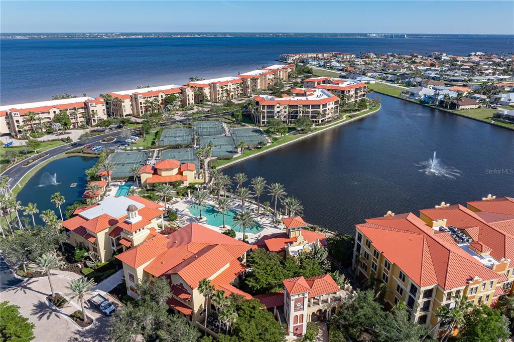 An aerial view of a waterfront residential complex featuring a pool, tennis courts, and buildings — 89 VIVANTE BOULEVARD UNIT 8943, PUNTA GORDA, FL