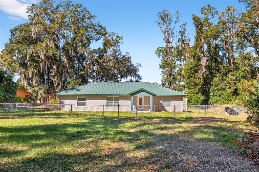 A single-story house with a green metal roof sits behind a chain-link fence — 201 N WEST STREET, INTERLACHEN, FL