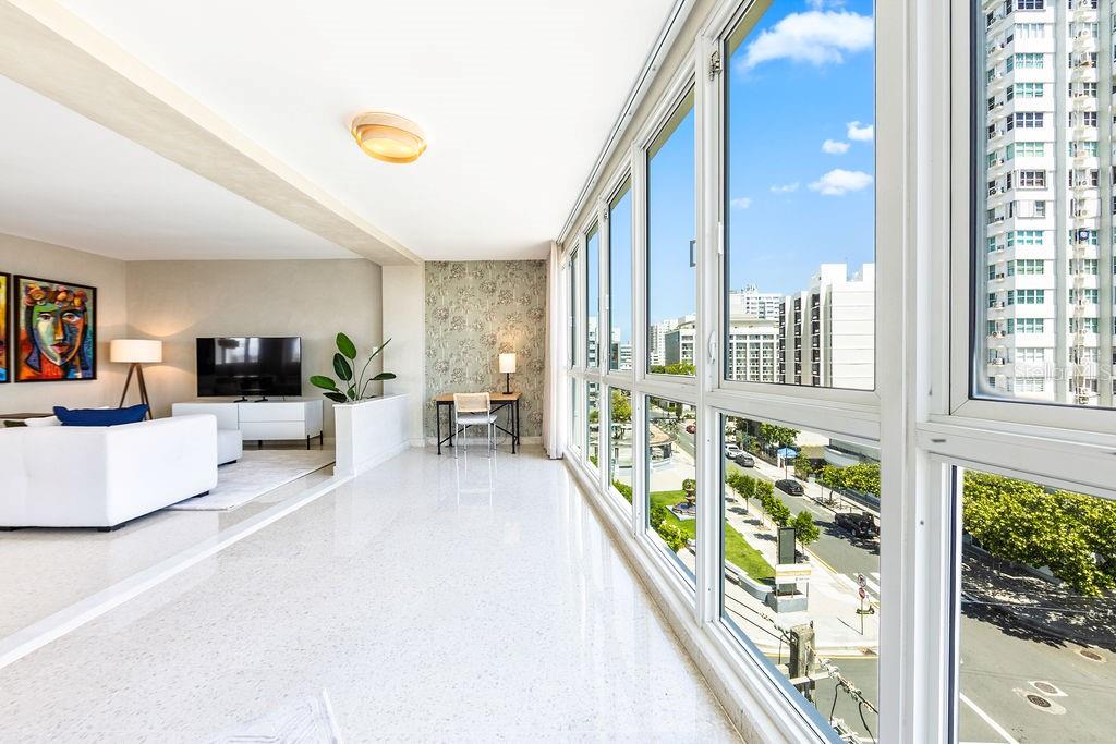 A bright living room with white floors, a desk area, and floor-to-ceiling windows overlooking streets — 57 ASHFORD AVENUE UNIT 5, SAN JUAN, PR