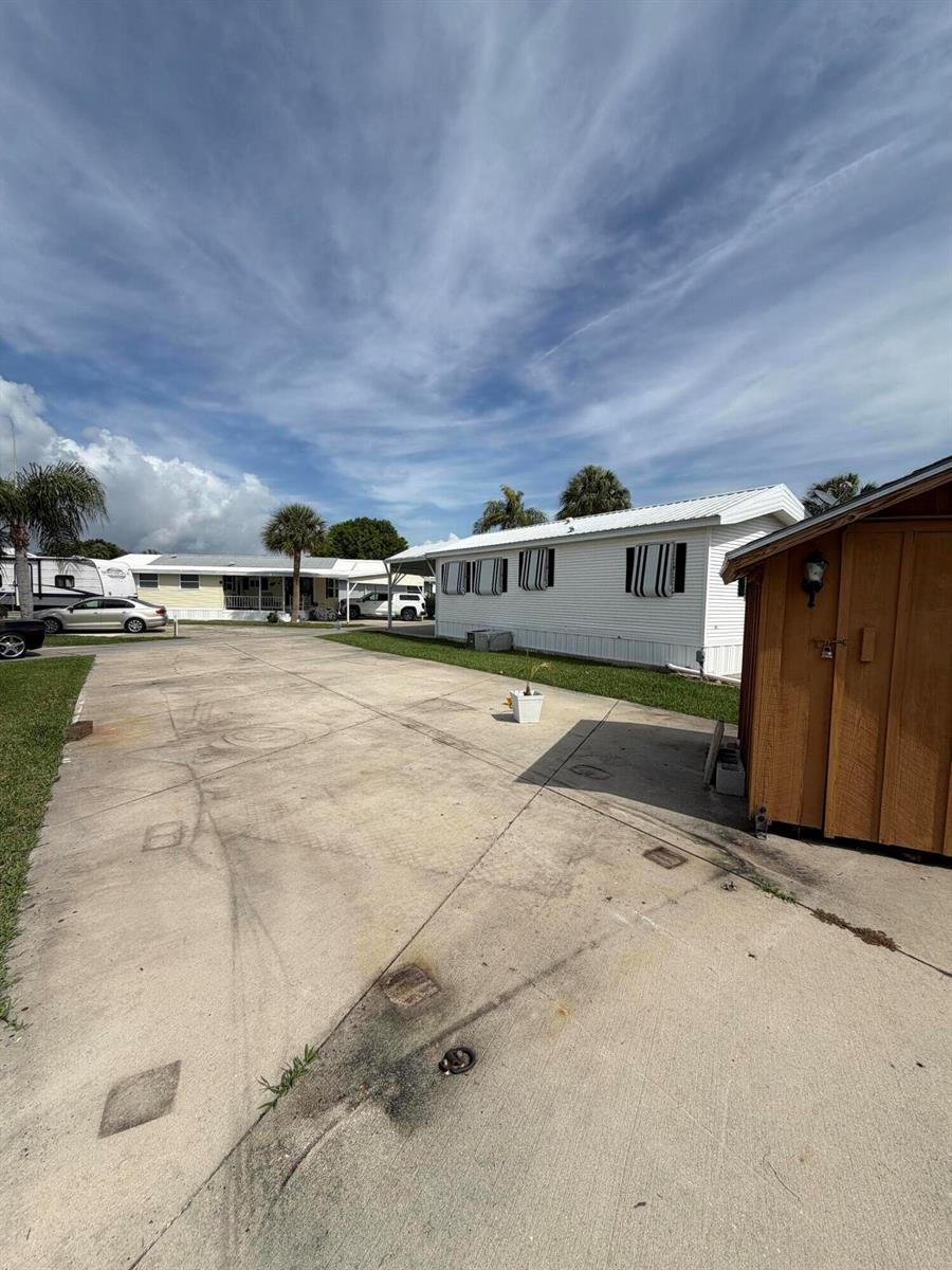 A concrete driveway leads to a white mobile home with a wooden shed nearby — 5340 SE 65th Terrace, Okeechobee FL 34974, OKEECHOBEE, FL