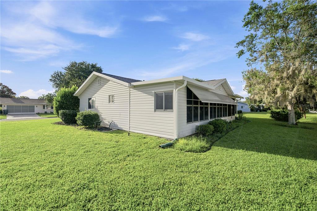 A side view of a light-colored, single-story house with a screened-in porch and large lawn — 17832 SE 96TH AVENUE, SUMMERFIELD, FL
