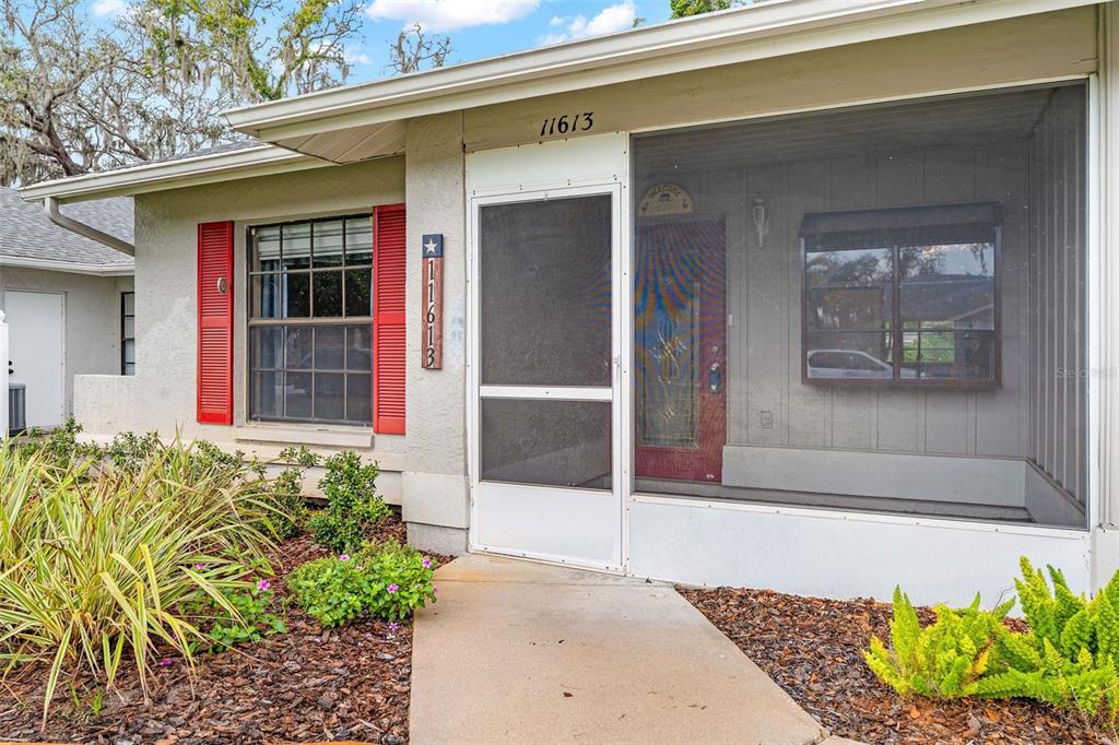 The exterior of a house features a screened-in porch, red shutters, and a concrete walkway — 11613 PEAR TREE DRIVE, NEW PORT RICHEY, FL