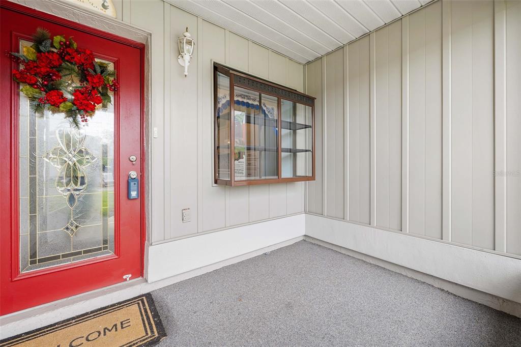 A covered porch features a red front door, a display cabinet, and light-colored siding — 11613 PEAR TREE DRIVE, NEW PORT RICHEY, FL