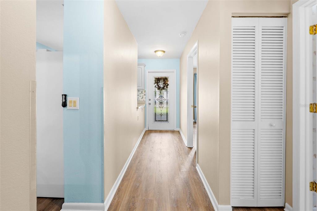 A hallway with wood-look flooring leads to a white front door with a glass insert — 11613 PEAR TREE DRIVE, NEW PORT RICHEY, FL