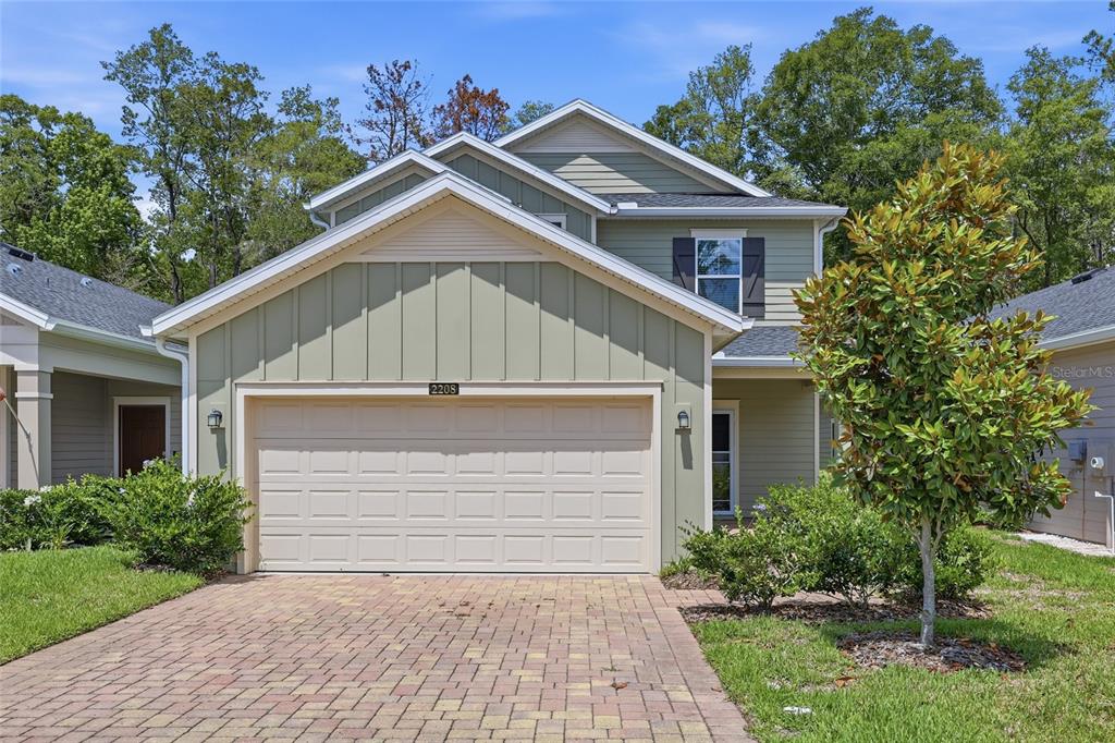 A two-story house with light green siding, a two-car garage, and a brick paver driveway — 2208 NW 89TH WAY, GAINESVILLE, FL