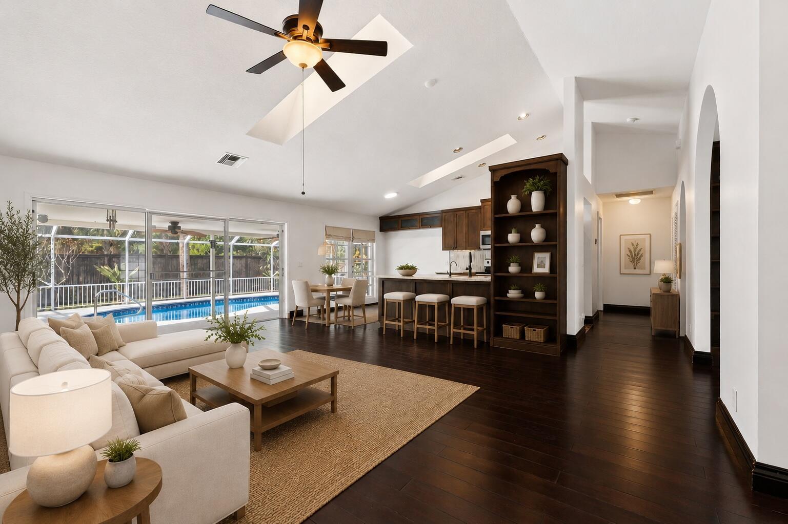 An open-concept living room and kitchen feature dark wood floors, vaulted ceilings, and pool views — 11480 150th Court N, FL 33478, FL