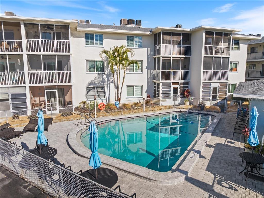 A swimming pool sits in the courtyard of a multi-story apartment building with screened balconies — 708 TAMIAMI TRAIL S UNIT 209, VENICE, FL
