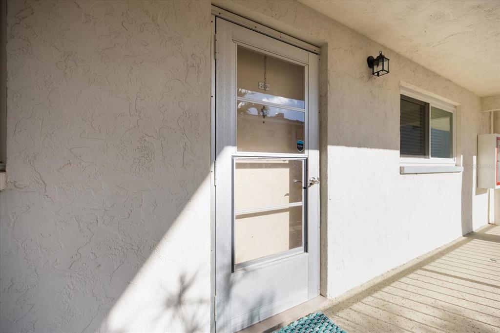 A white exterior door with a glass storm door sits on a concrete walkway — 708 TAMIAMI TRAIL S UNIT 209, VENICE, FL