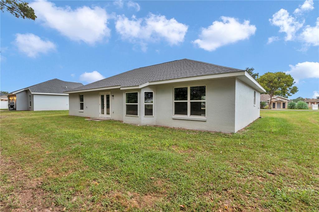 The exterior rear view of a single-story house with a lawn and glass doors — 6711 SW 64TH AVENUE, OCALA, FL
