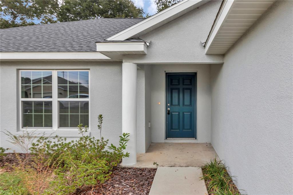 A light gray house exterior features a blue front door and a white support column — 6711 SW 64TH AVENUE, OCALA, FL