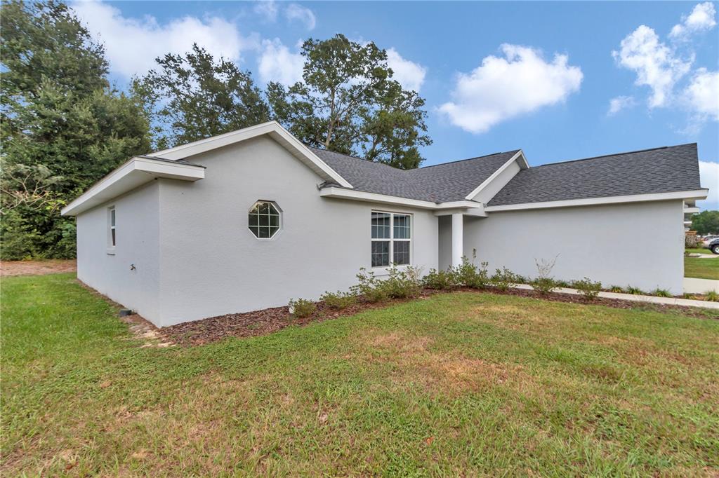The exterior of a light gray, single-story house features a dark shingled roof and landscaping — 6711 SW 64TH AVENUE, OCALA, FL