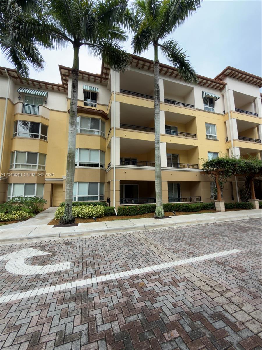 A multi-story apartment building features yellow stucco walls, balconies, and tall palm trees — 16100 Emerald Estates Dr # 281, Weston FL 33331, WESTON, FL