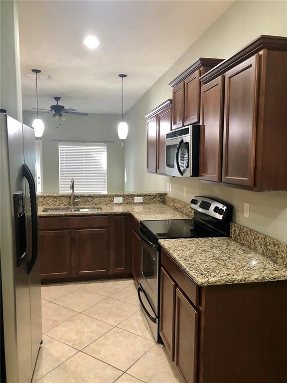 A kitchen features dark wood cabinets, granite countertops, stainless steel appliances, and tile flooring — 8541 BRUSHLEAF WAY, TAMPA, FL