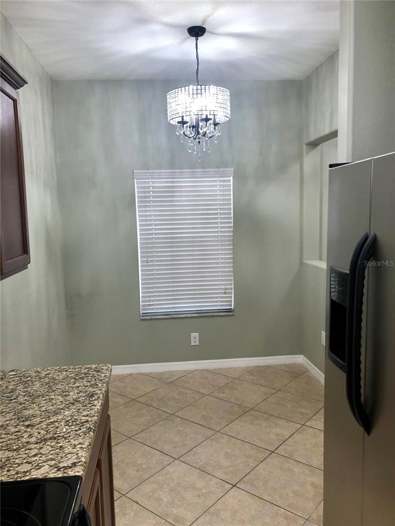 A kitchen dining area features tile flooring, a crystal chandelier, and a window with blinds — 8541 BRUSHLEAF WAY, TAMPA, FL