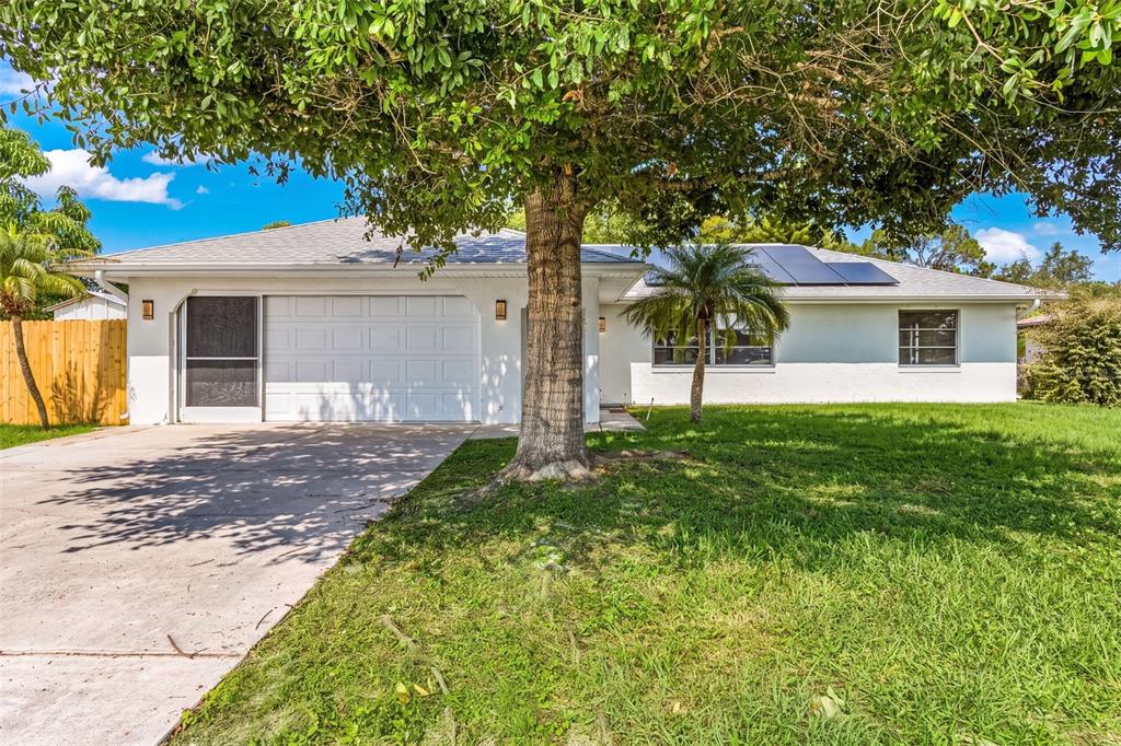 A single-story white house with a garage, solar panels, and a large tree in front — 1128 INVERNESS STREET, PORT CHARLOTTE, FL