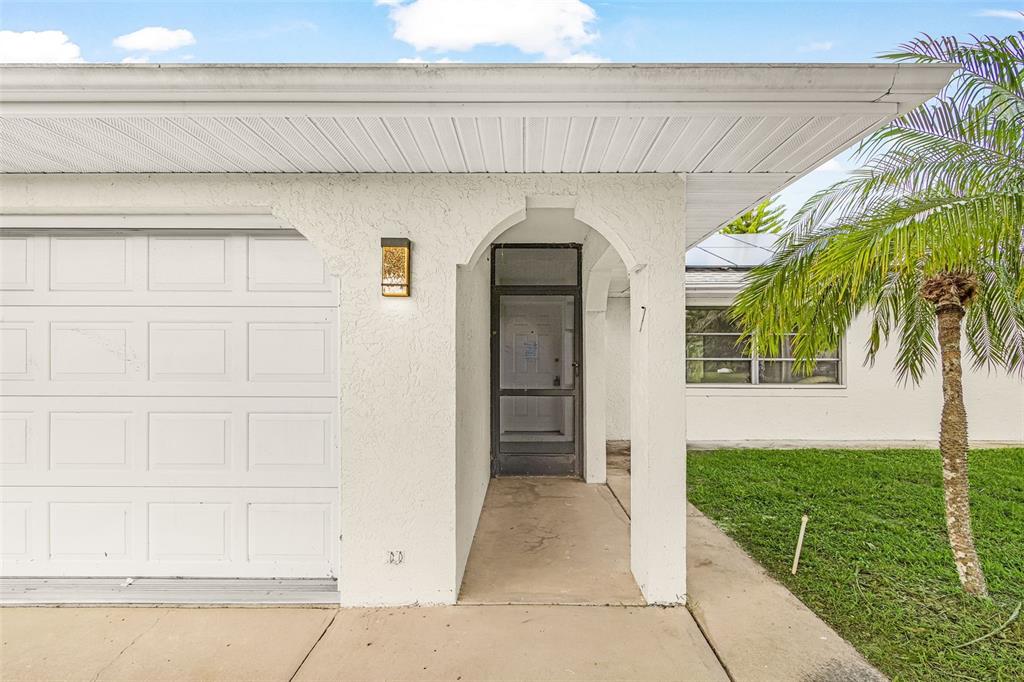 The exterior of a white house features a garage, a covered entryway, and a palm tree — 1128 INVERNESS STREET, PORT CHARLOTTE, FL