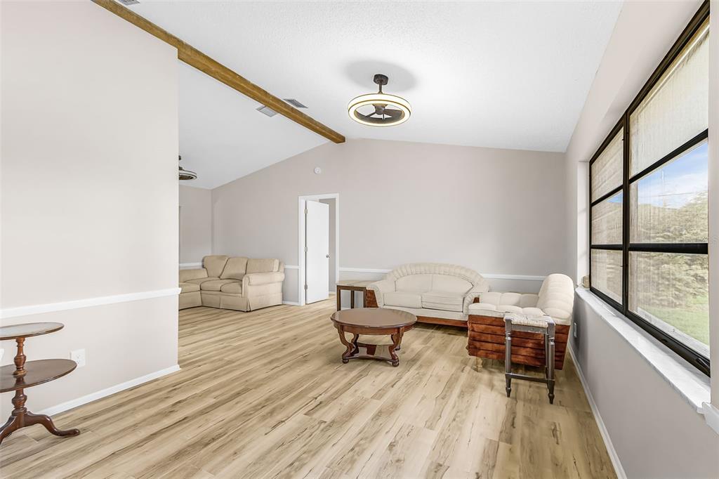 A living room with light wood-look flooring, a vaulted ceiling, and a wooden ceiling beam — 1128 INVERNESS STREET, PORT CHARLOTTE, FL