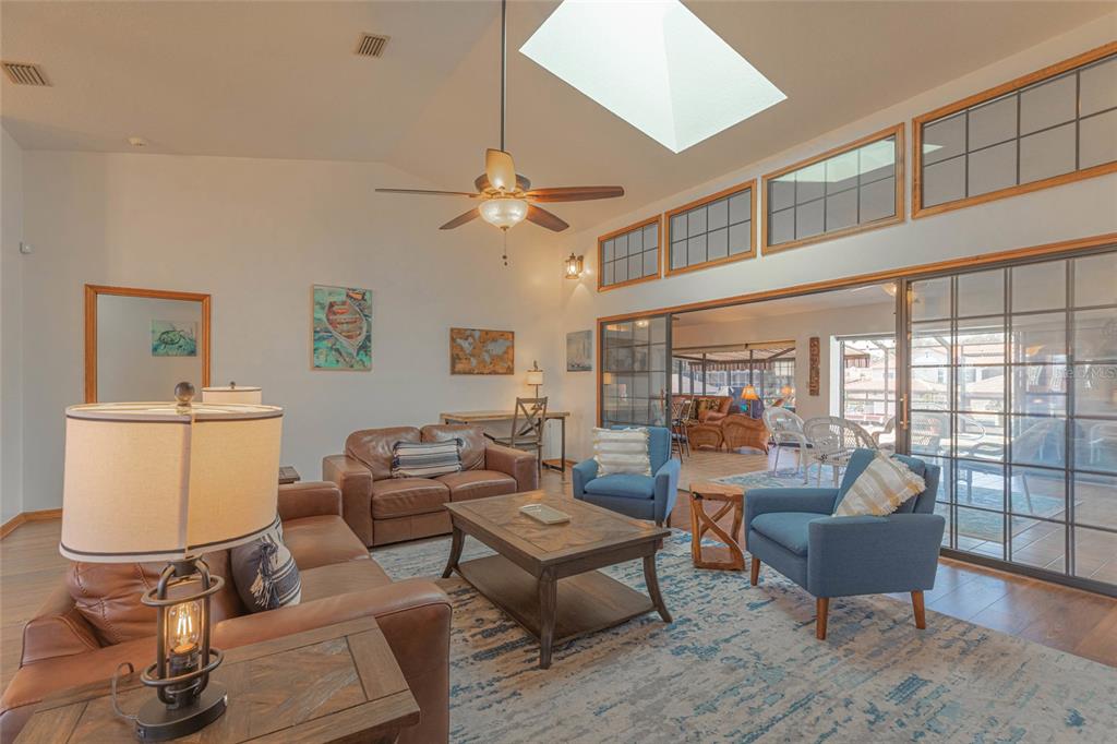 A living room features leather sofas, blue armchairs, a skylight, and sliding glass doors — 27 CHERRYTREE COURT, PALM COAST, FL