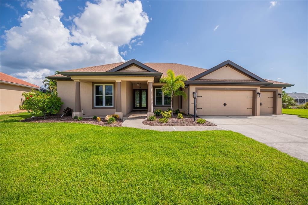 A single-story suburban house with a tan stucco exterior, a three-car garage, and a lawn — 8730 MYSTIC CIRCLE, NORTH PORT, FL