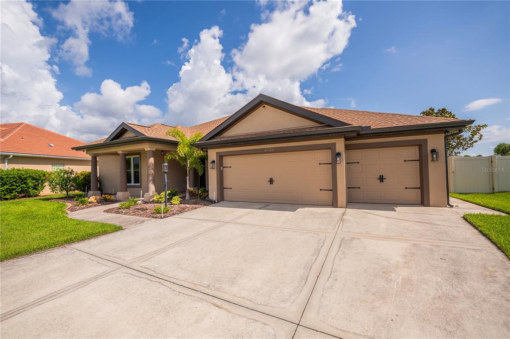 A tan single-story house features a three-car garage and a concrete driveway under a sky — 8730 MYSTIC CIRCLE, NORTH PORT, FL