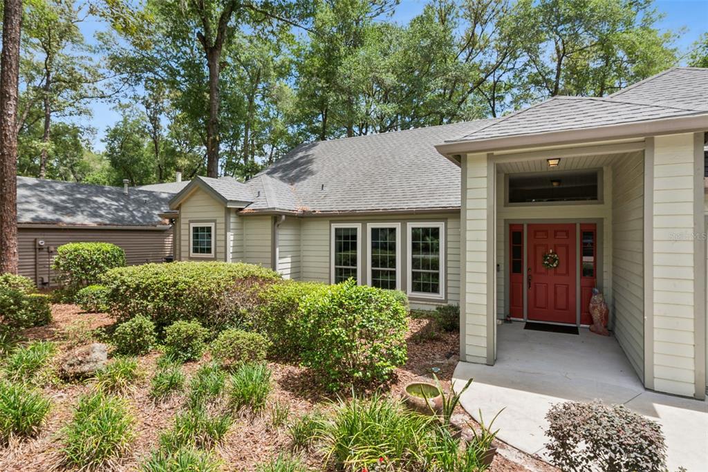 A single-story house with light siding, a red front door, and a landscaped front yard — 10525 SW 55TH PLACE, GAINESVILLE, FL