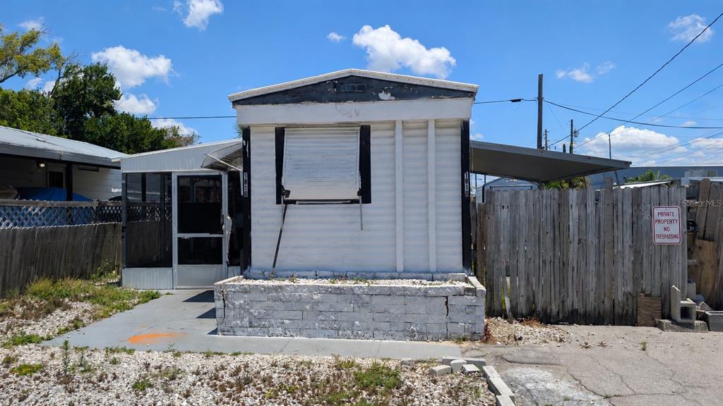 A white mobile home with a screened porch and a stone planter sits behind a fence — 1810 HOLIDAY DRIVE, HOLIDAY, FL