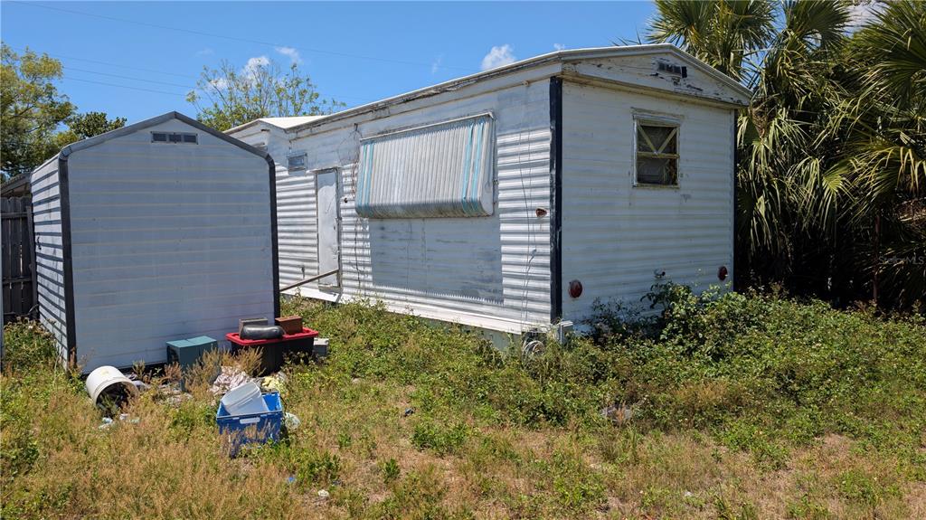 An exterior view of a weathered mobile home and a small shed on a grassy lot — 1810 HOLIDAY DRIVE, HOLIDAY, FL
