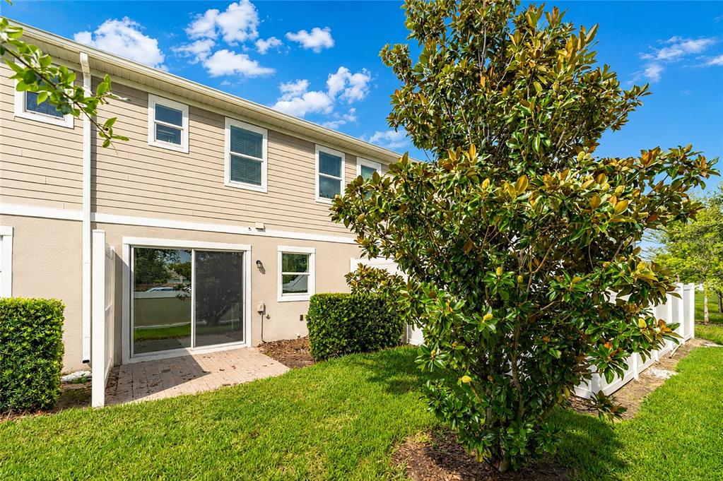 The exterior of a two-story townhouse features beige siding, a sliding glass door, and landscaping — 2342 SEDGE GRASS WAY, ORLANDO, FL