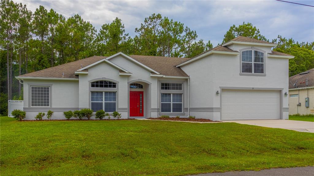 A single-story house with white stucco walls, a red front door, and a two-car garage — 13 ZINNIA TRAIL, PALM COAST, FL