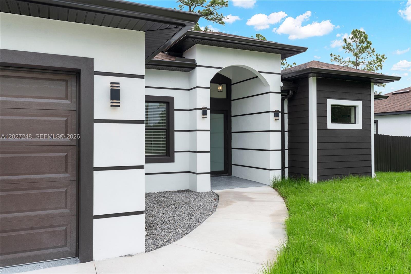 The exterior of a modern house features white walls with black horizontal trim accents — 1047 E Merry St, Lehigh Acres FL 33974, LEHIGH ACRES, FL